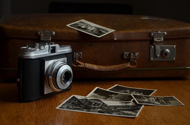 Ein schwarzsilberner Fotoapparat vor einem braunen Lederkoffer. Davor liegen einige Schwarz-Weiß-Fotografien.
