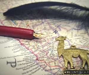 Ausschnitt einer historischen Landkarte von Peru. Darauf liegen (von hinten nach vorne) eine schwarze Feder, eine Kalligraphie-Feder und ein Messinganhänger in Form eines Vicuñas, ein mit Lamas verwandter Neuweltkamelide.